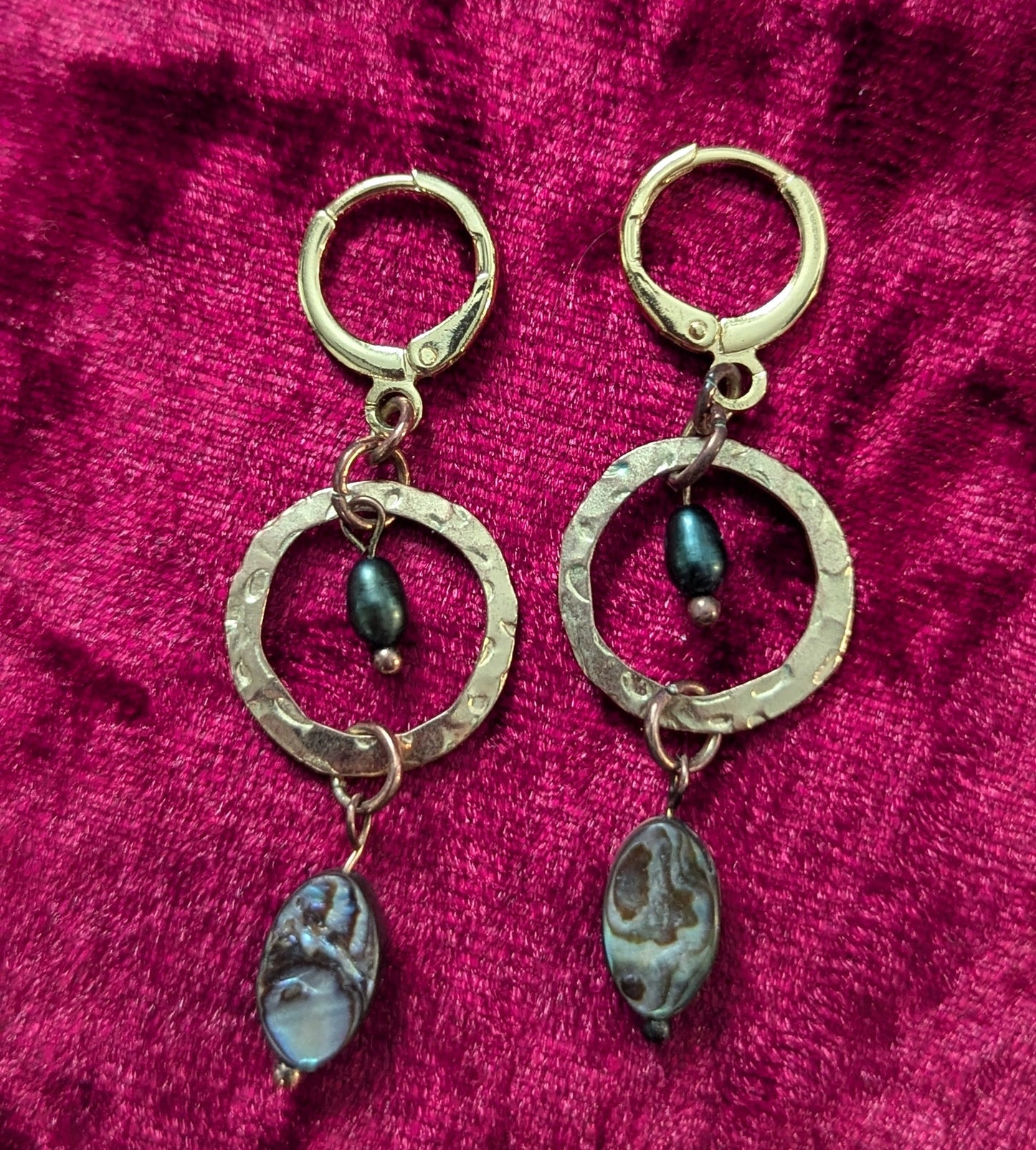 Gold earrings with circular designs on a red textured fabric background