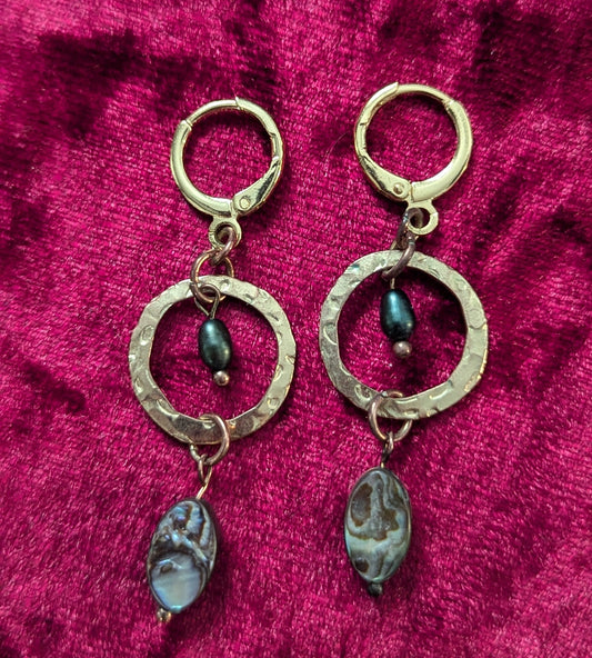 Gold earrings with circular designs on a red textured fabric background