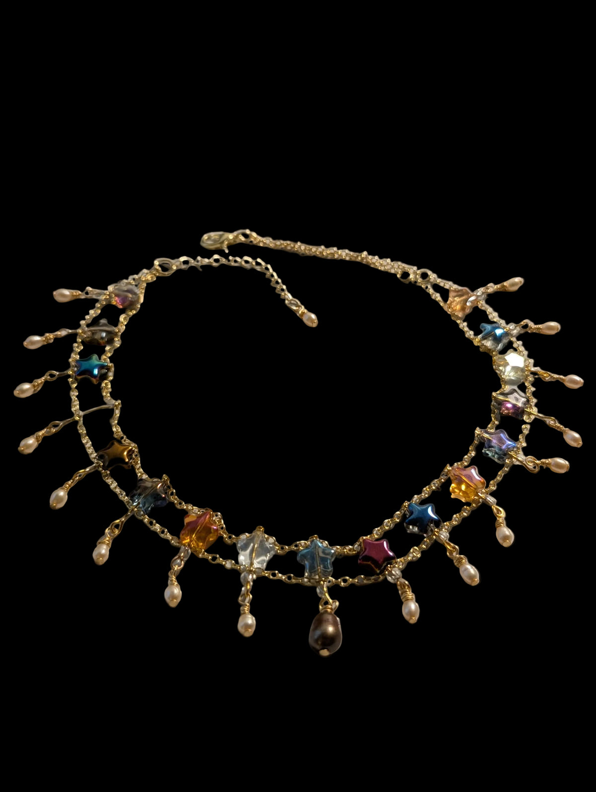 A gold-tone chain necklace with dangling charms, featuring colorful faceted gemstones and small pearl-like beads, displayed on a light gray surface.