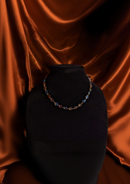 A delicate beaded necklace with small multicolored beads on a black velvet jewelry bust, set against a draped brown satin fabric background.