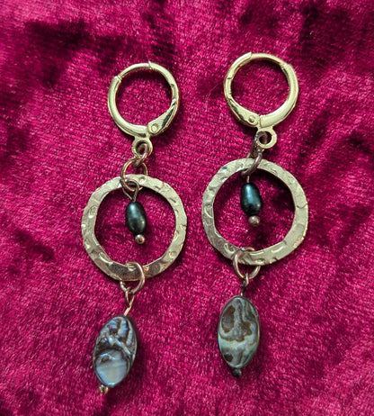 Gold earrings with circular designs on a red textured fabric background