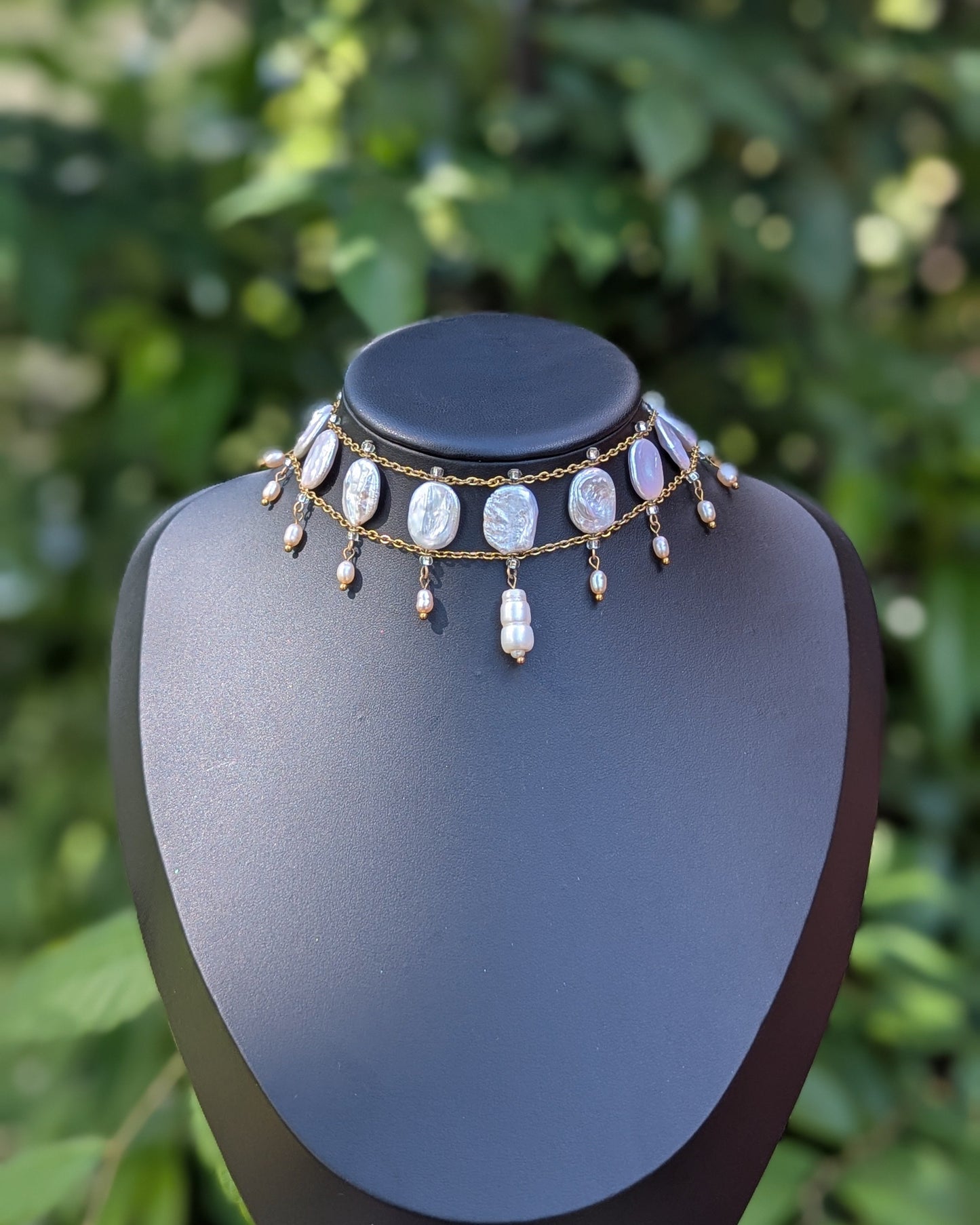 baroque pearl necklace on a mannequin bust with a green leafy background